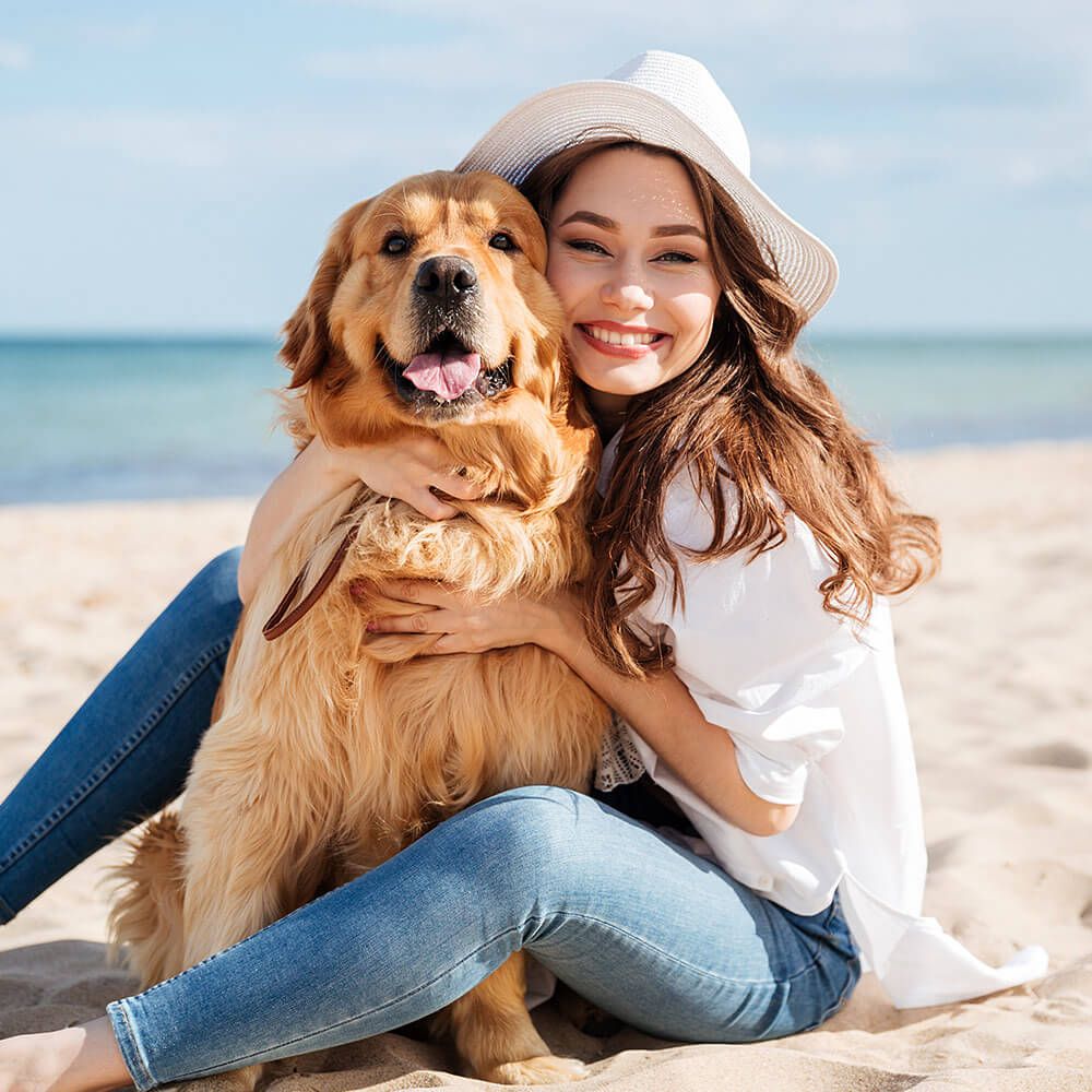 Woman sitting on the beach with a golden retriever, both smiling. happy about shopping from snuggypet